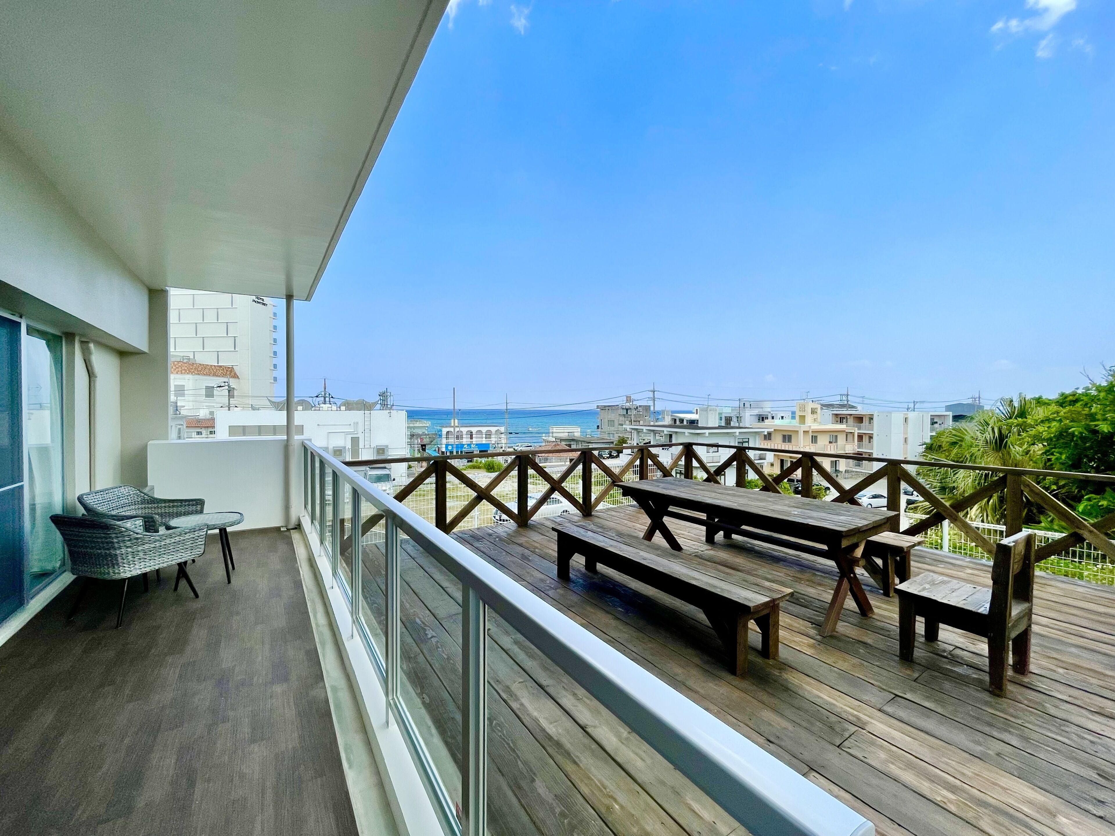 Un balcon doté d’un plancher en bois, de rampes en métal, de chaises en osier et de tables en bois.