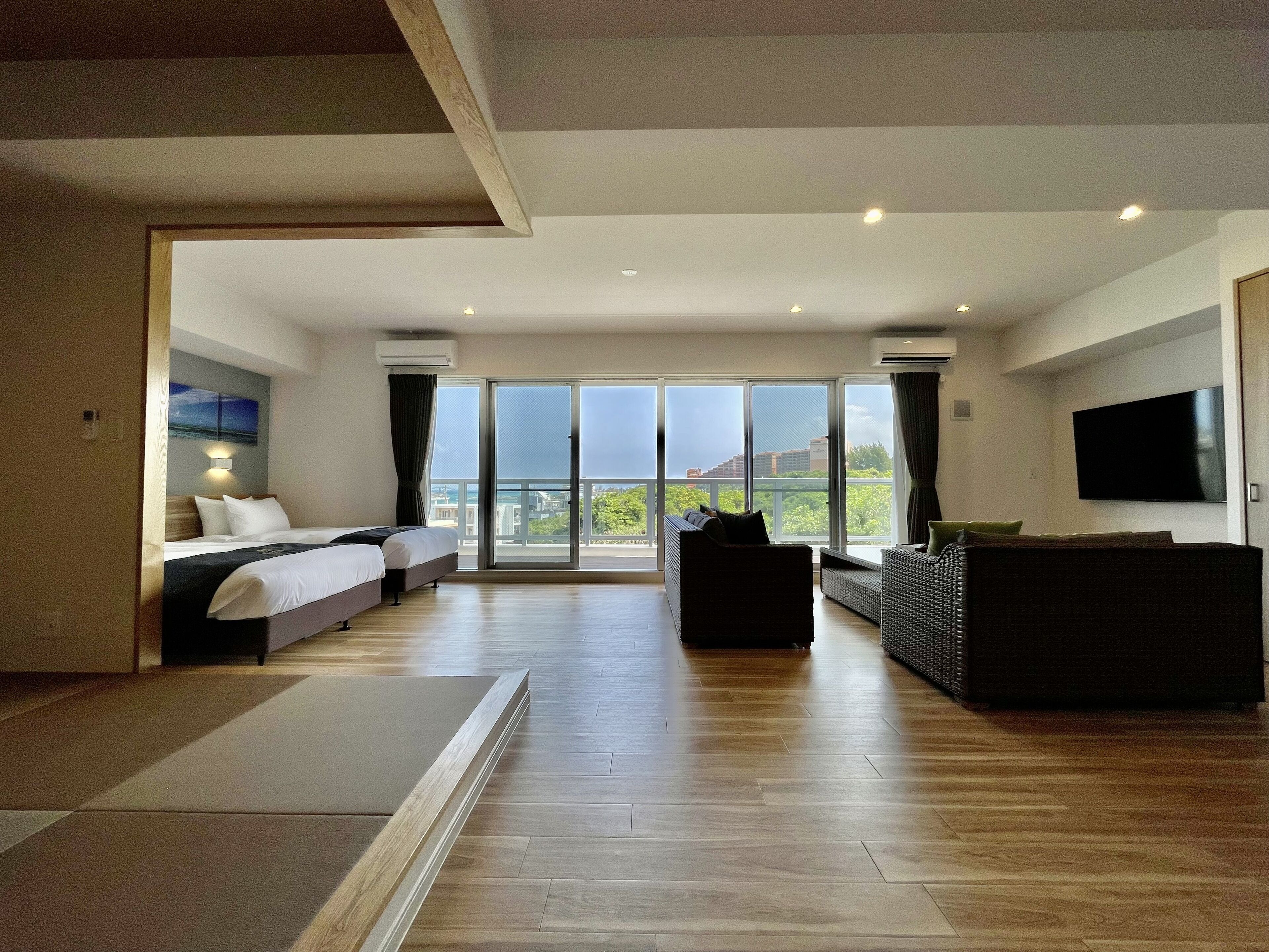 Ein modernes Hotelzimmer mit einem großen Bett, einer Couch, einem Fernseher und einem Balkon mit Blick auf die Stadt.