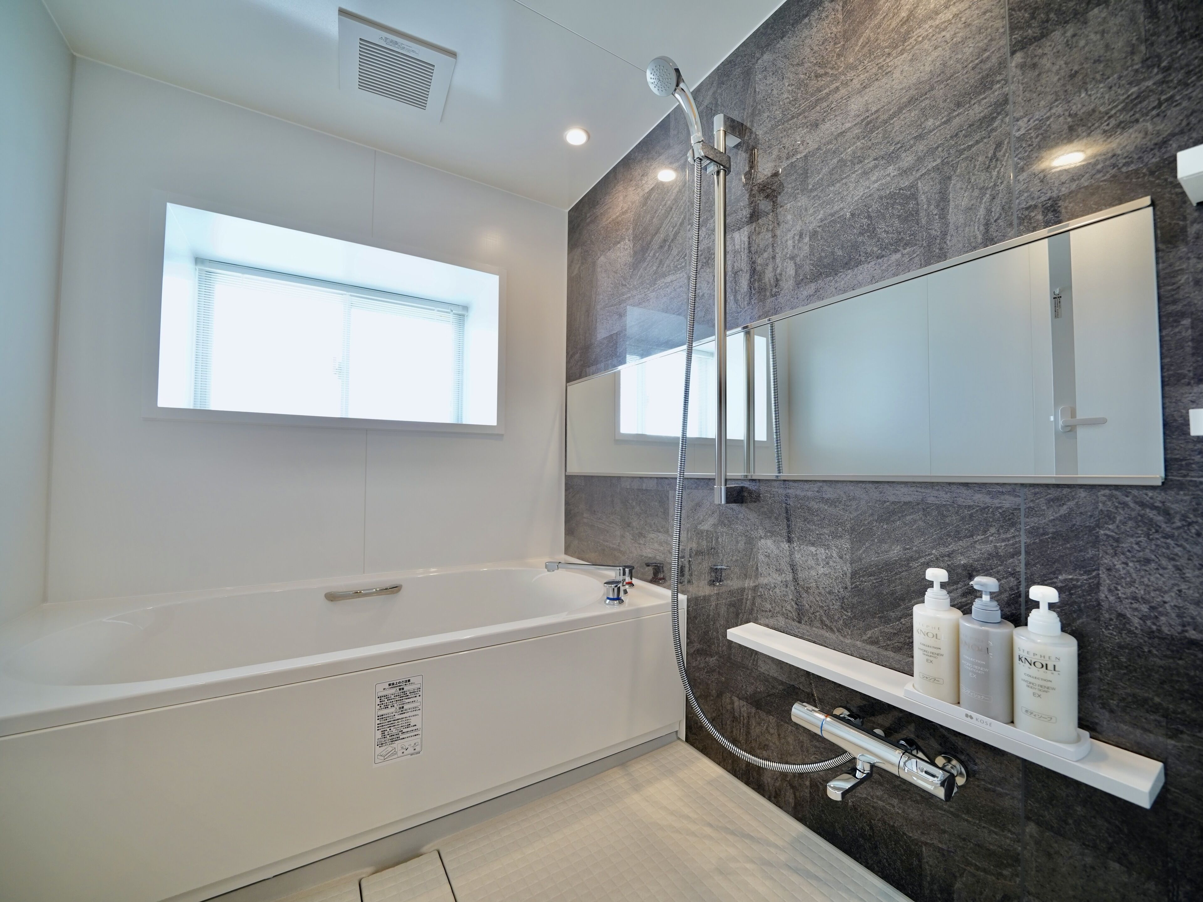 A modern bathroom with a bathtub, a shower, a large mirror, and a window.