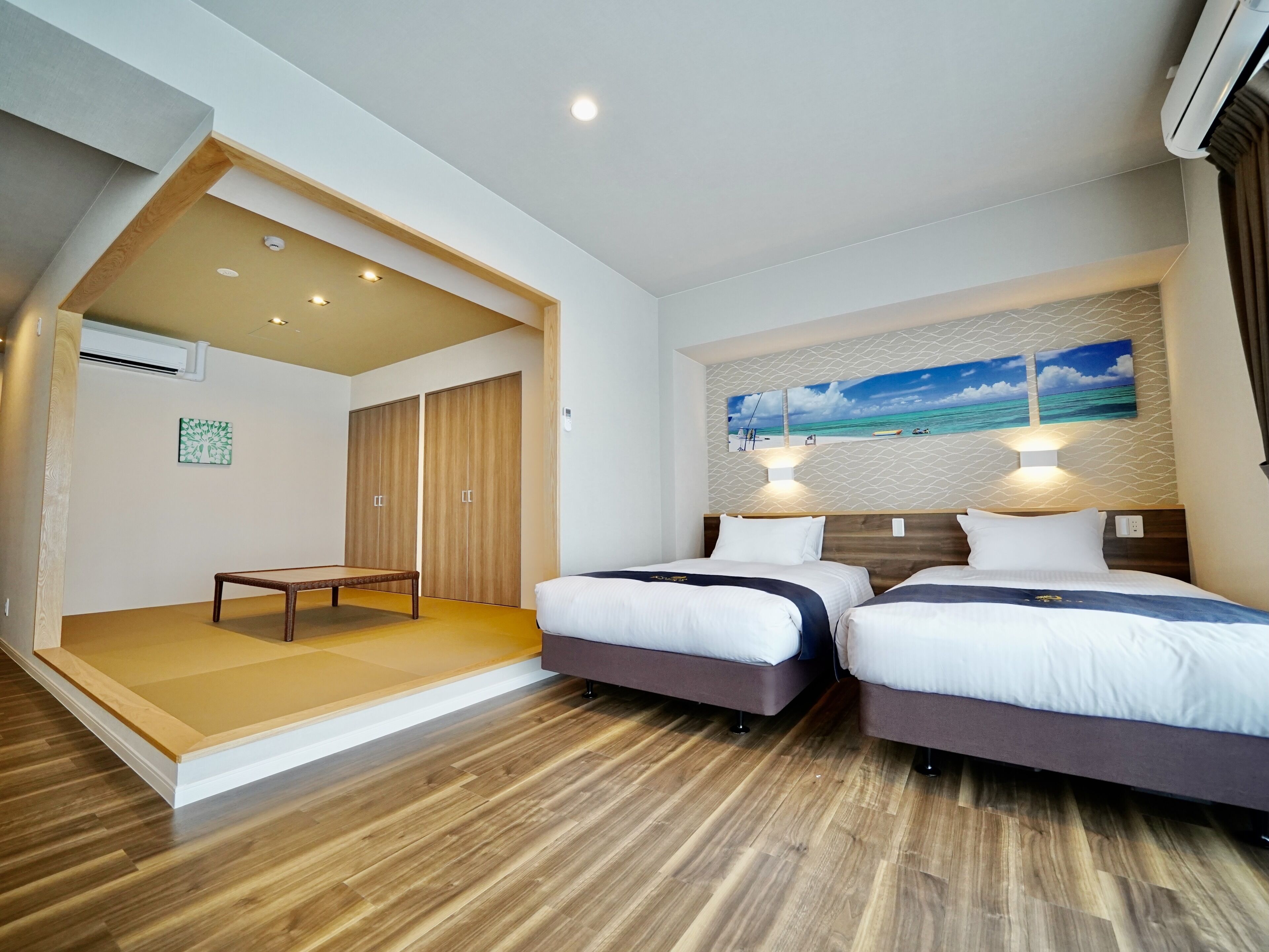 Een moderne hotelkamer met twee bedden, een klein tafeltje en een schilderij van een strandgezicht.
