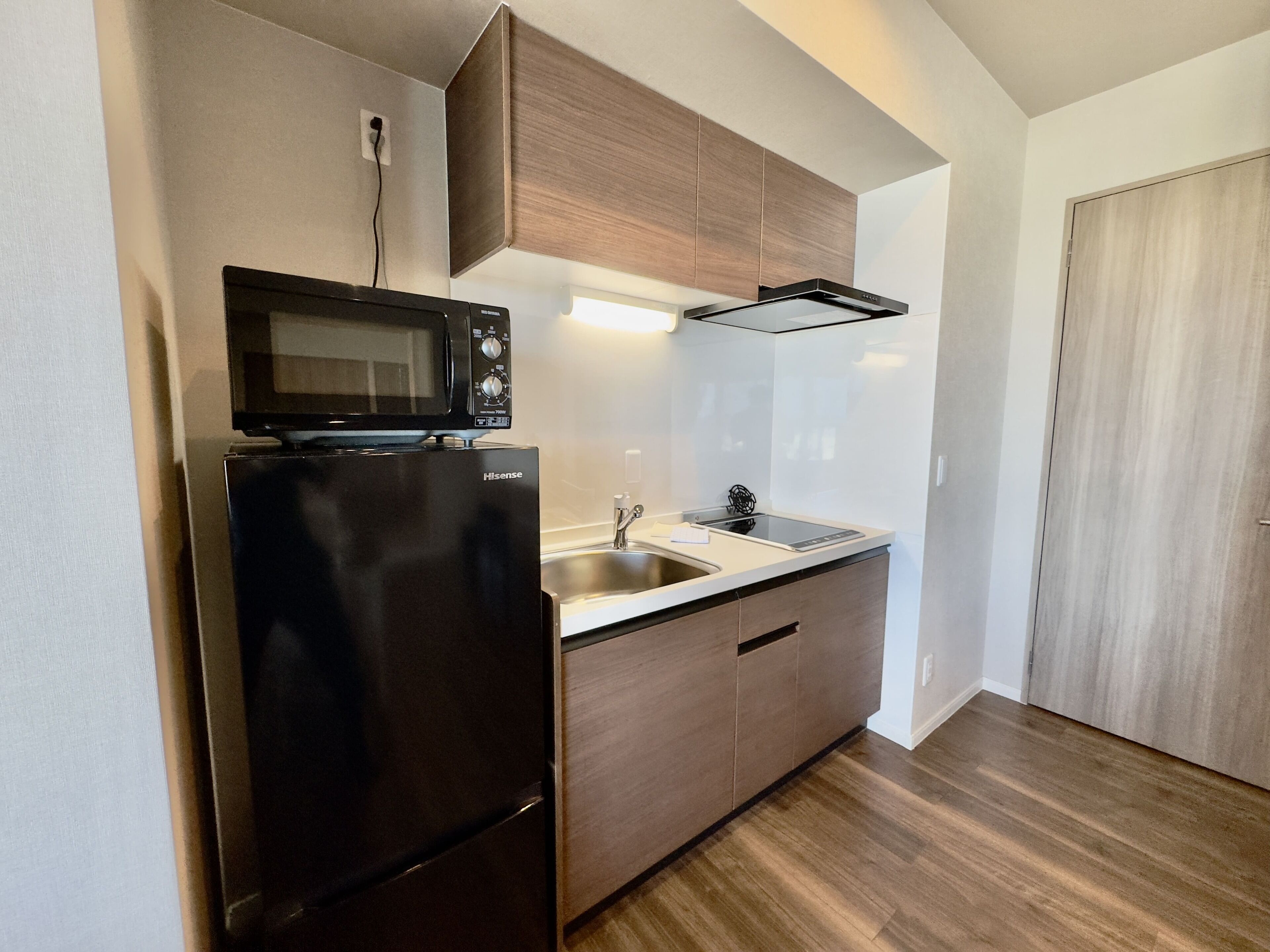 A compact kitchen with a black refrigerator, a microwave, a sink, and wooden cabinets.