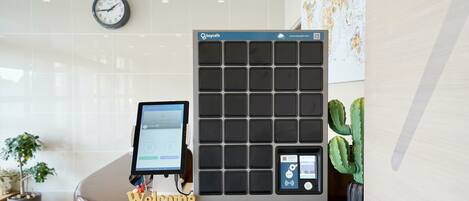 Un mostrador de recepción de hotel con un quiosco digital, un reloj, un cartel de bienvenida y una planta de cactus.