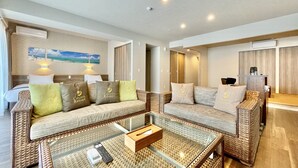 A modern hotel room with a sofa set, a glass coffee table, and a painting of a beach scene. - Coral Palace Onna by Sunset Avenue (Onna)