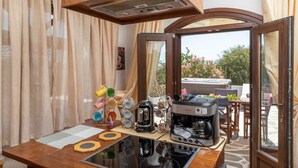 A kitchen with a stove, coffee maker, and a dining area with chairs and a table. - Villa Parisi Naxos Deluxe 2 (Ναξος Αγκίδια)