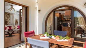 A dining area with a wooden table and chairs, a sofa, and a kitchen visible through an arched doorway. - Villa Parisi Naxos Deluxe 2 (Ναξος Αγκίδια)