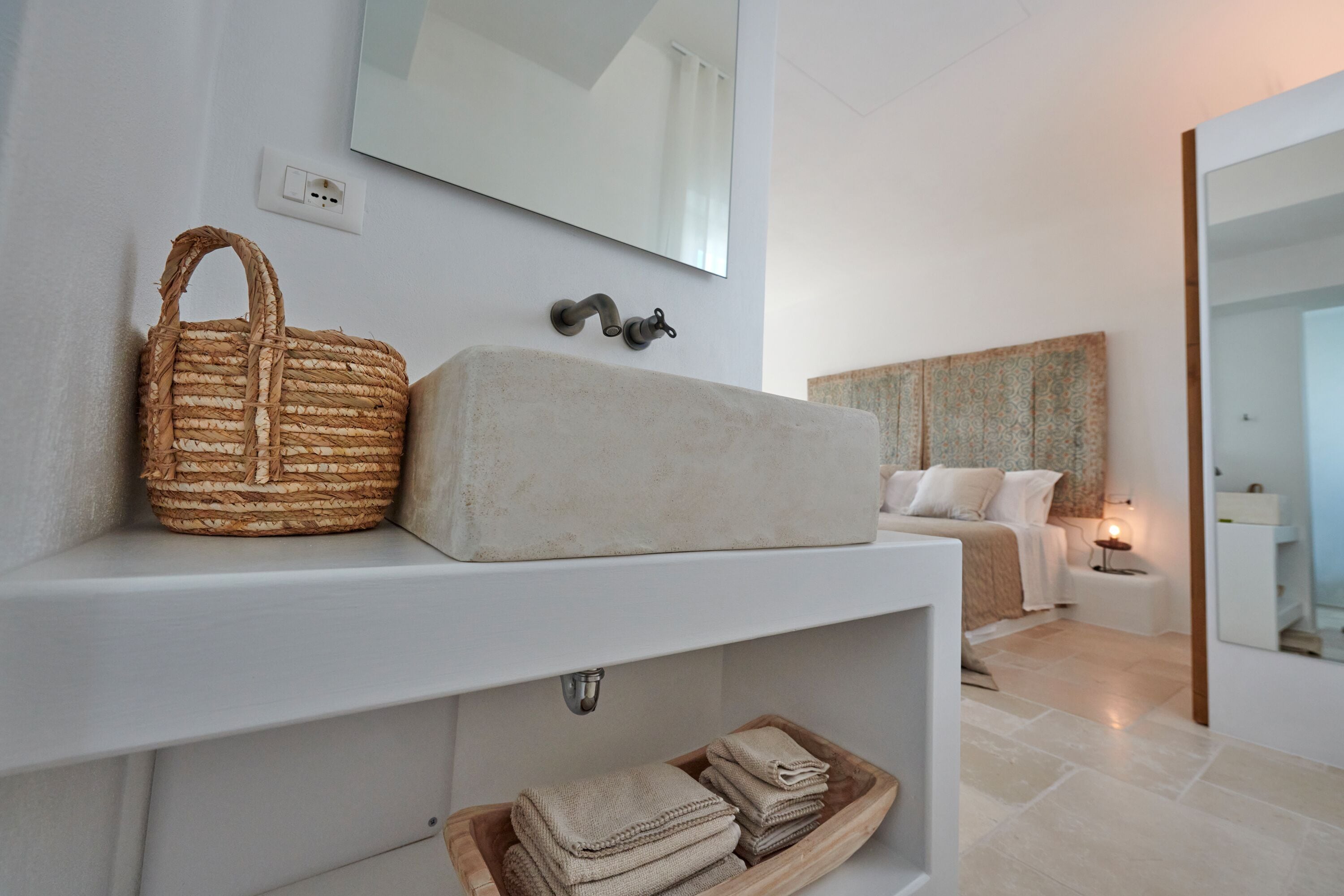 Une salle de bain moderne avec un grand miroir, un panier en osier, un lavabo beige et des serviettes soigneusement pliées sur une étagère.