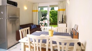A compact kitchen with a refrigerator, a dining table with chairs, a sofa, and a window with curtains. - Residence Limoni del Rustichel: Apartment N.1 with lake view, underground parking and pool. (Toscolano Maderno)