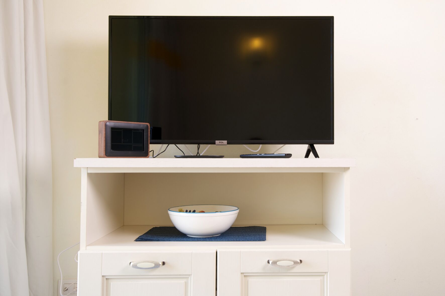 A TV on a white stand with a bowl on a blue mat below it.