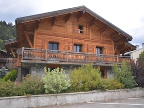 A wooden chalet with a balcony, stone foundation, and surrounded by greenery. - Charming Studio Near Village Center, 150m from Slopes, Balcony, Pet-Friendly (Les Gets)
