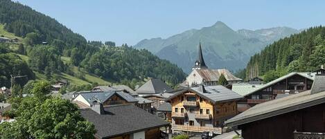 A mountain village with traditional wooden buildings, a church, and a view of the surrounding mountains.