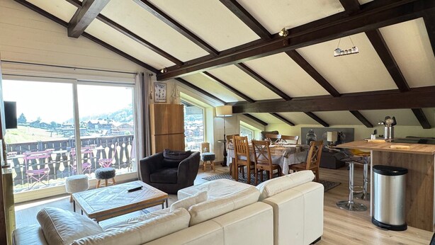 A spacious living area with a high ceiling, wooden beams, a large sofa, dining table, and chairs.