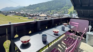A terrace with a table set for dining, overlooking a town and mountains.