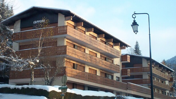 A multi-story hotel with balconies, a sign indicating 'Sapporo', and snow on the ground. - Charming Apartment Near Slopes with Balcony, Parking, and Modern Amenities (Les Gets)