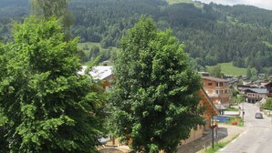 A view of a town with a prominent building in the foreground, surrounded by lush green hills and a clear sky. - Charming Apartment Near Slopes with Balcony, Parking, and Modern Amenities (Les Gets)