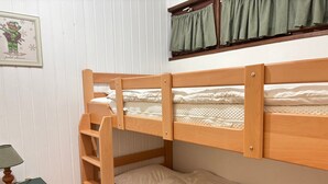 A bunk bed with a wooden frame, a small table with a lamp, and a window with curtains. - Central Apartment in Les Gets, Steps from Village and Slopes (Les Gets)