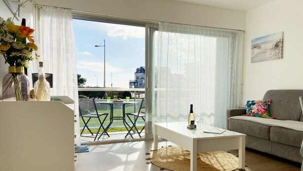 Una sala moderna con un piso de vidrio que da a un balcón, una mesa de centro blanca, un sofá gris y un cuadro en la pared.