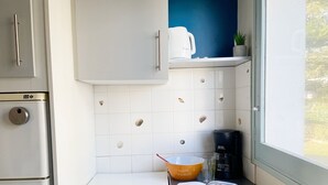 Una cocina compacta con estufa blanca, cafetera y una pequeña estantería con una planta.