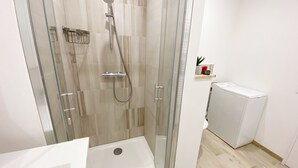 Un baño moderno con ducha de vidrio, lavamanos blanco y un estante pequeño con artículos de tocador.