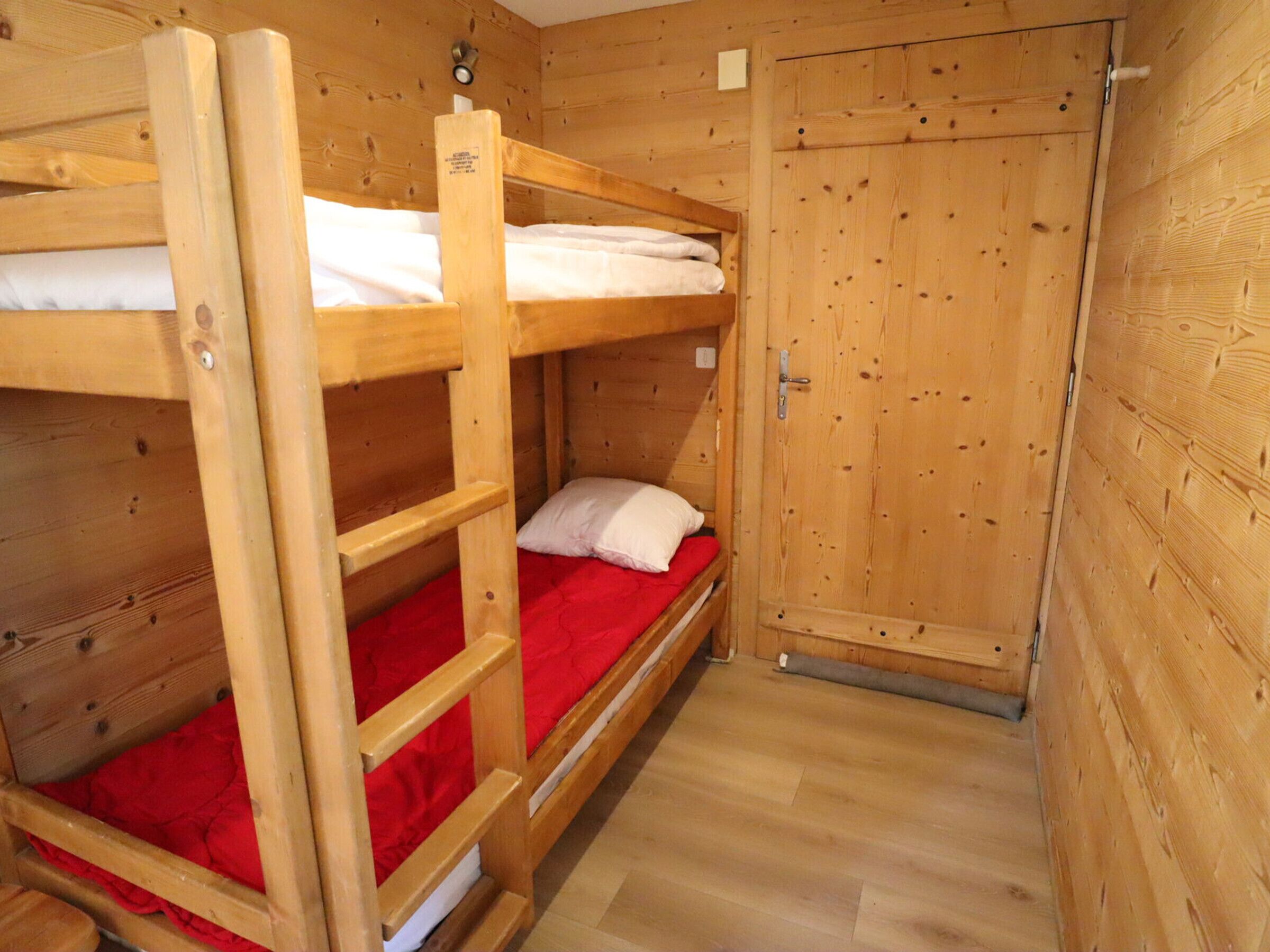 Une chambre avec un lit superposé en bois, un matelas rouge, une armoire en bois et un plancher en bois.