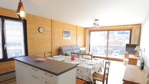 Ein gemütliches Blockhaus mit Essbereich, Küche und großem Fenster mit Blick auf die Berge.