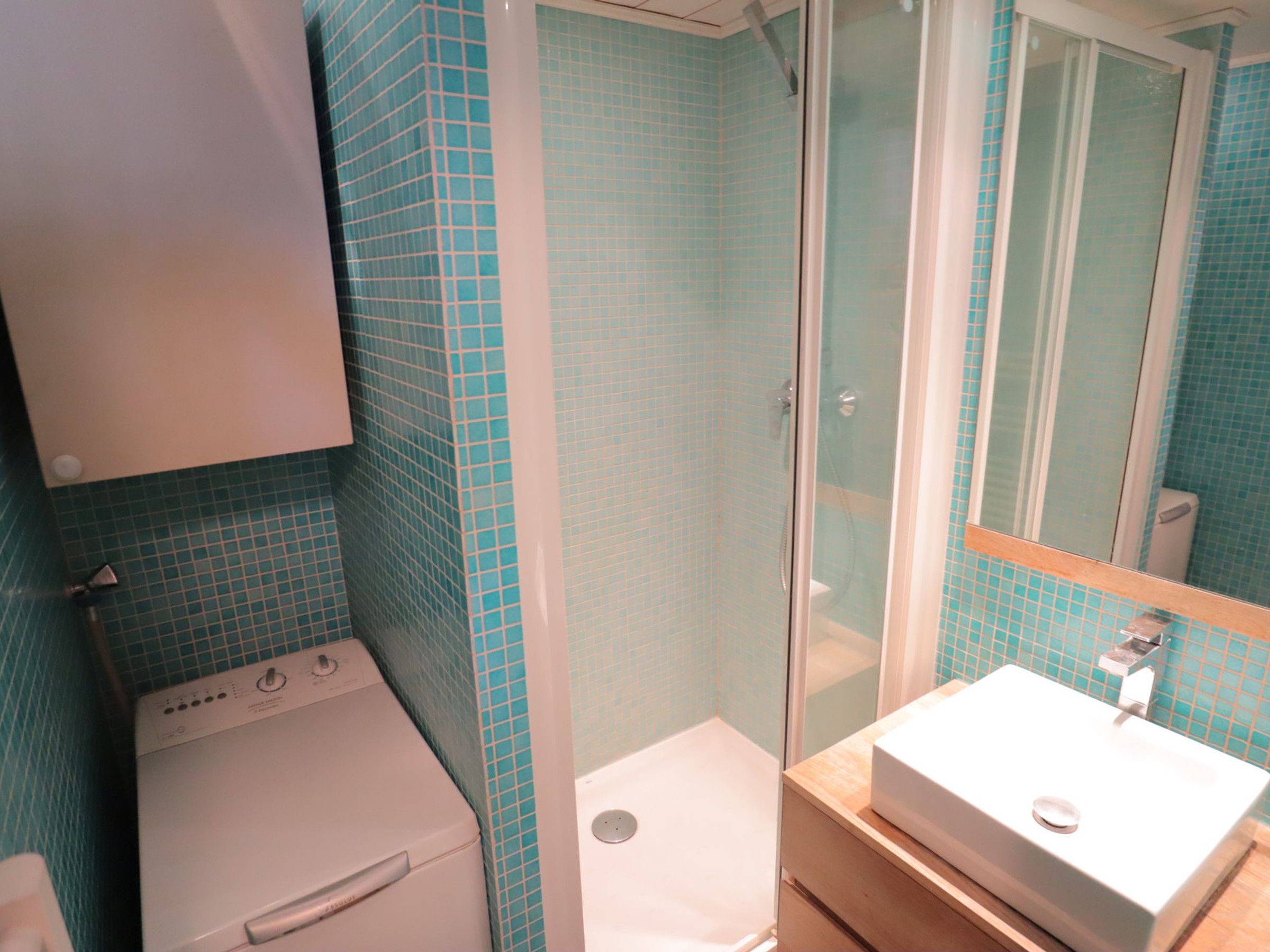 A bathroom with a white washing machine, a glass-enclosed shower, and a sink with a mirror above it.