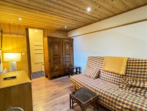 A cozy room with a wooden ceiling, a checkered sofa, a small table, and a cabinet.
