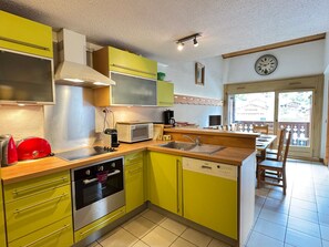 A kitchen with a microwave, stove, and sink, and a dining area with chairs and a table. - Spacious 3-bedroom apartment in Les Gets, near center and slopes, parking included (Les Gets)