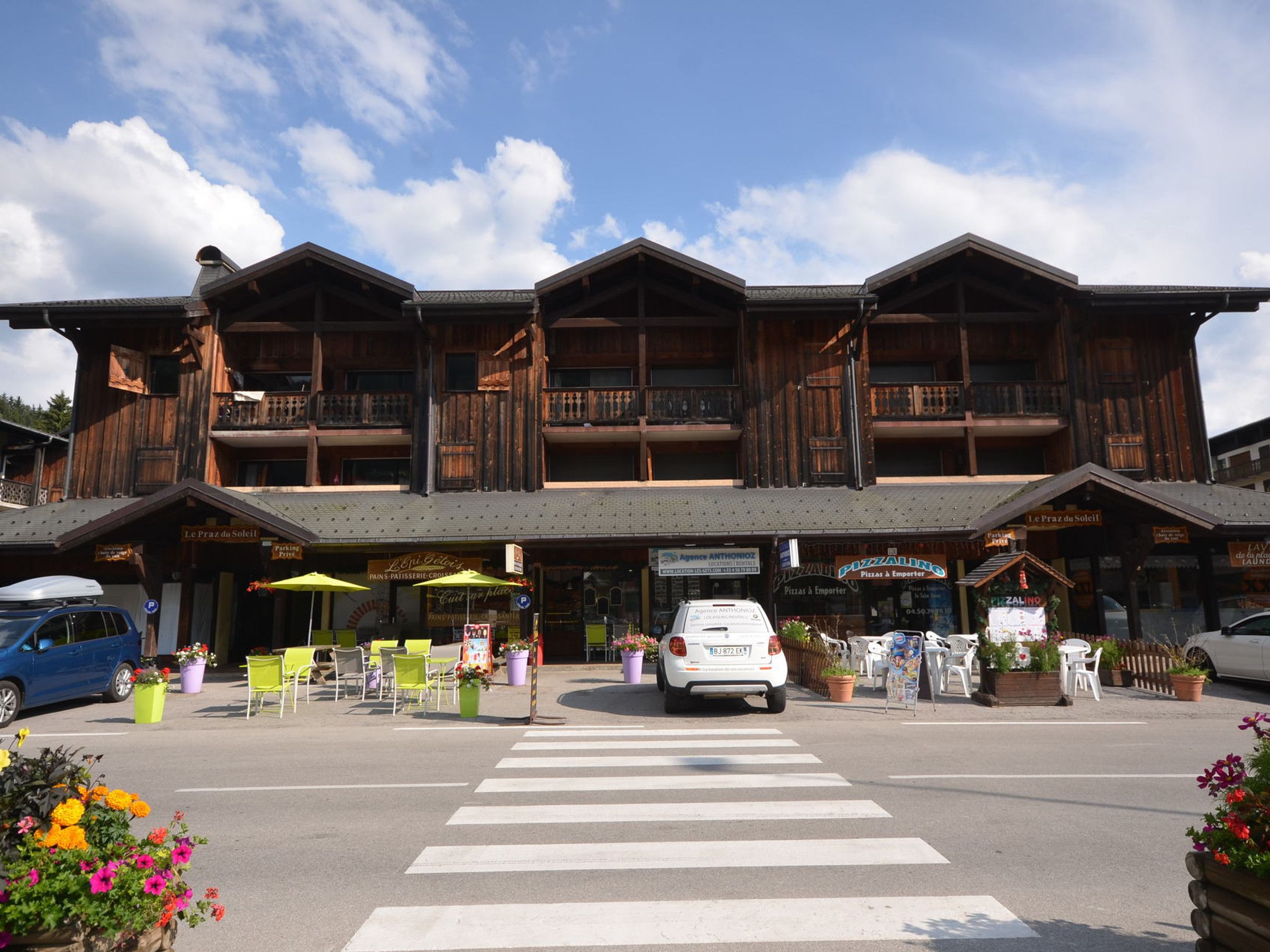 A wooden building with balconies, a crosswalk, and outdoor seating.
