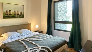 A bedroom with a bed, a nightstand, a lamp, a window with curtains, and a painting of sheep on the wall. - Les Gets - Appartement dans une résidence neuve (Les Gets)