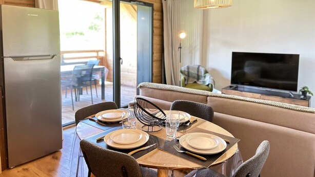 A dining area with a table set for four, a sofa, a TV, and a refrigerator. - Les Gets - Appartement dans une résidence neuve (Les Gets)