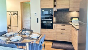 A modern kitchen with wooden cabinets, a built-in oven, microwave, and a refrigerator. There is a dining table set with plates and glasses. - Les Gets - Appartement dans une résidence neuve (Les Gets)