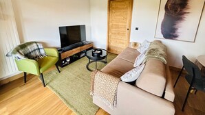 A modern living room with a TV, sofa, and green armchair. - Les Gets - Appartement dans une résidence neuve (Les Gets)
