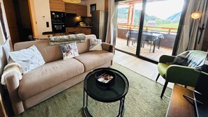 A modern living room with a sofa, coffee table, and a view of a deck and mountains. - Les Gets - Appartement dans une résidence neuve (Les Gets)
