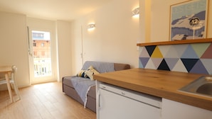 Ett kompakt bostadsutrymme med ett litet kök, en soffa, ett matbord och utsikt över omgivningen.