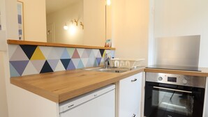 Ett kompakt kök med en bänkskiva i trä, en inbyggd tvättmaskin, en ugn i rostfritt stål och ett färgglatt, geometriskt mönstrat stänkskydd.
