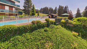 A hotel with a swimming pool, surrounded by lush greenery and a mountainous backdrop. - Ski-In/Ski-Out Studio with Pool, Tennis & Mountain Views - 1km from Les Gets Center (Les Gets)