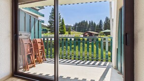 A balcony with a view of a green fence, trees, and a building in the background. - Ski-In/Ski-Out Studio with Pool, Tennis & Mountain Views - 1km from Les Gets Center (Les Gets)