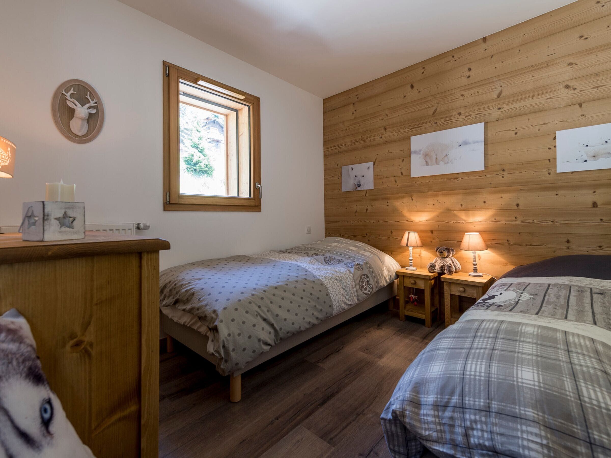 A cozy bedroom with two single beds, wooden walls, a window, and a wooden dresser.