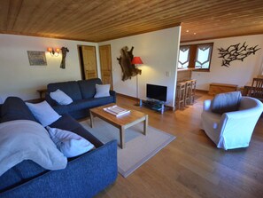 Uma sala de estar aconchegante com um sofá, poltrona e mesa de centro. Há uma televisão e um abajur no aposento.