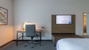 A hotel room with a bed, a desk with a chair, a television mounted on the wall, and a framed picture on the wall.
