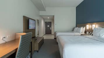 Een hotelkamer met een bureau, twee bedden, een televisie en een deur naar een gang.