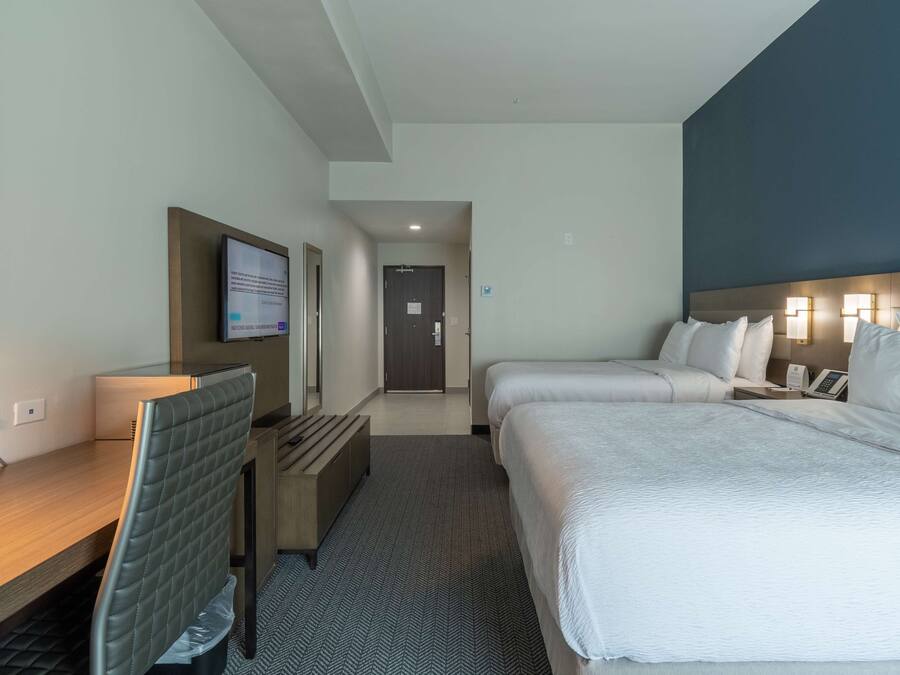A hotel room with a desk, two beds, a TV, and a door leading to a hallway.