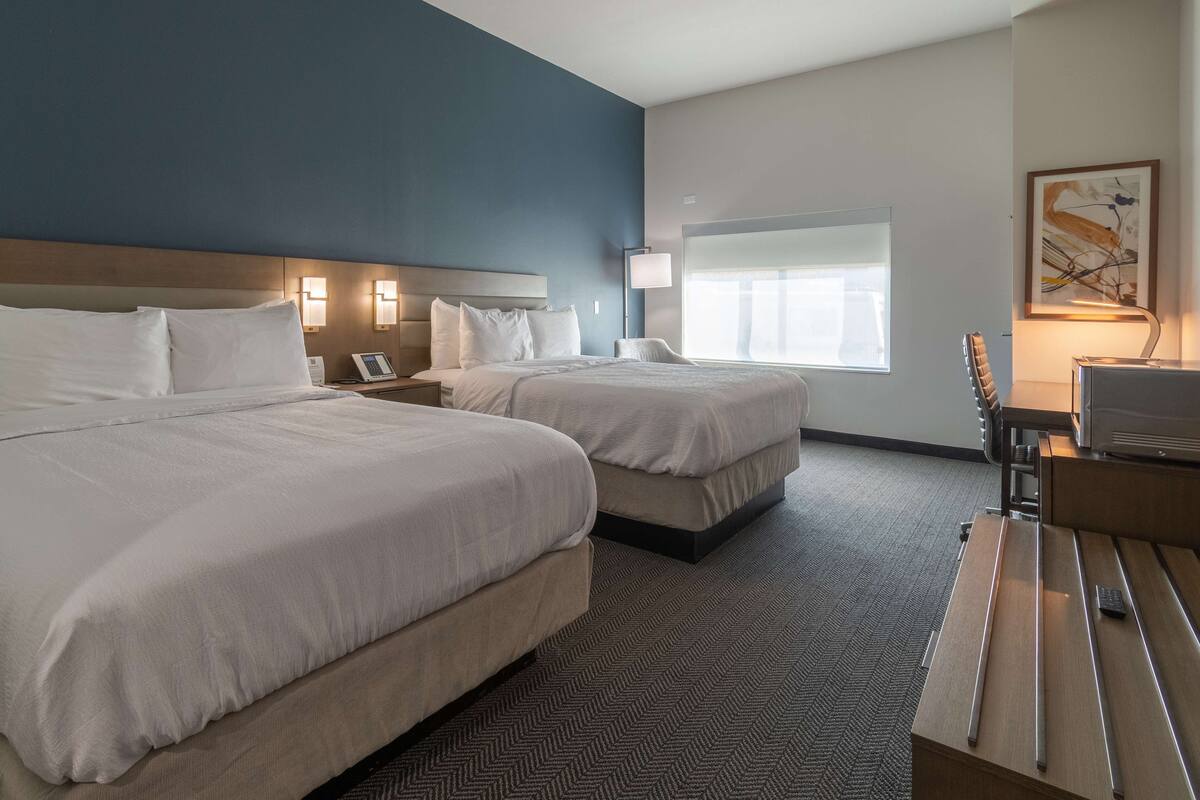 Een hotelkamer met twee bedden, een bureau, een lamp, een televisie en een raam met jaloezieën.