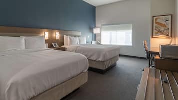 A hotel room with two beds, a desk, a lamp, a TV, and a window with blinds.