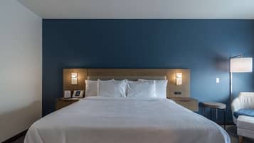 Una habitación de hotel con una cama grande, lámparas de noche, una mesita de noche, una silla y una lámpara en la pared.