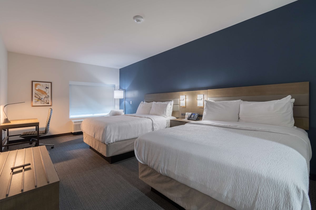 Een hotelkamer met twee bedden, een bureau, een stoel en een raam.