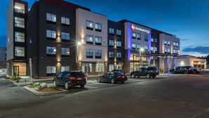 Un hotel moderno con varios pisos, estacionamiento y señalización iluminada.