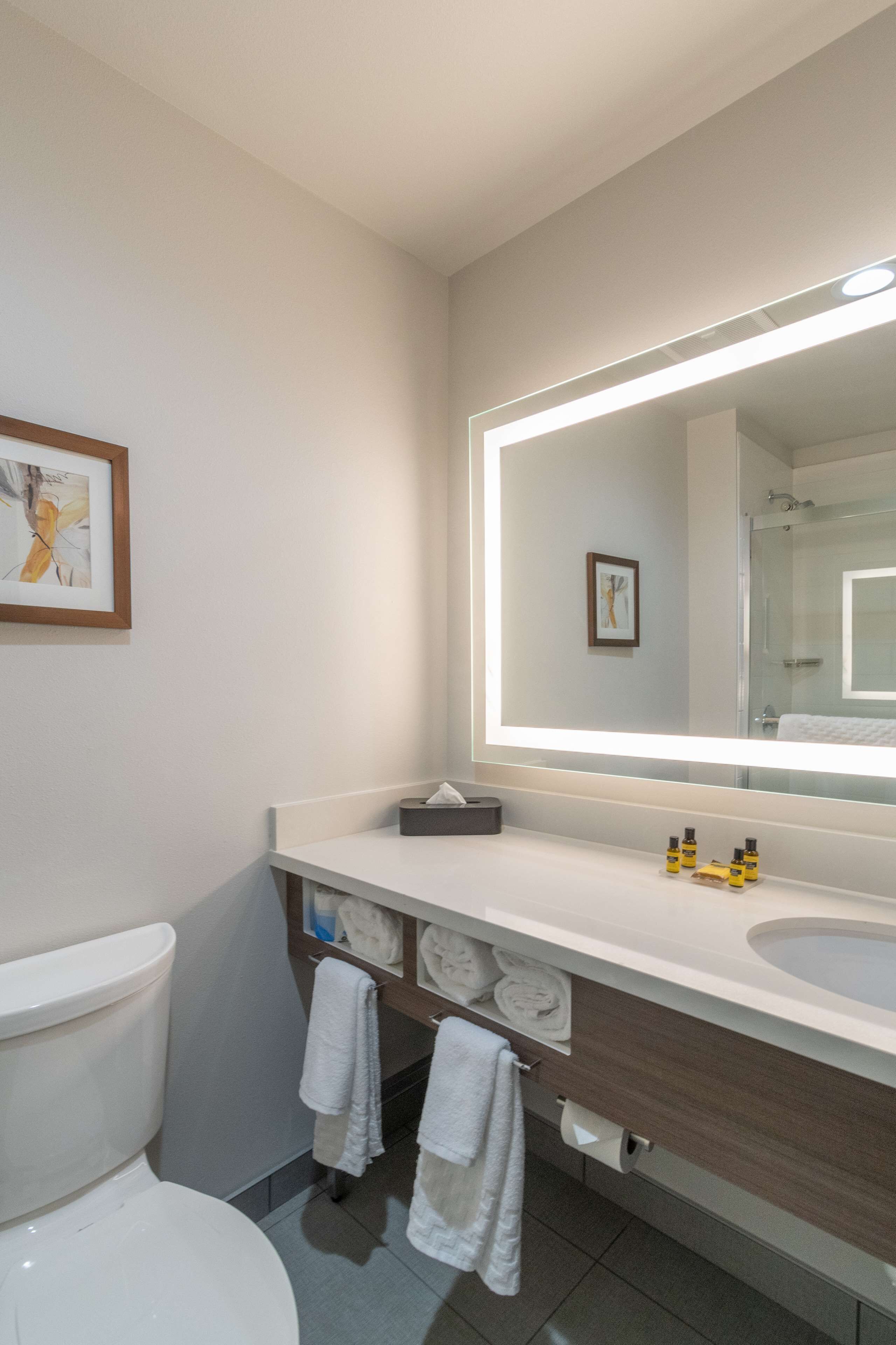 A modern bathroom with a large mirror, white fixtures, and neatly arranged towels.