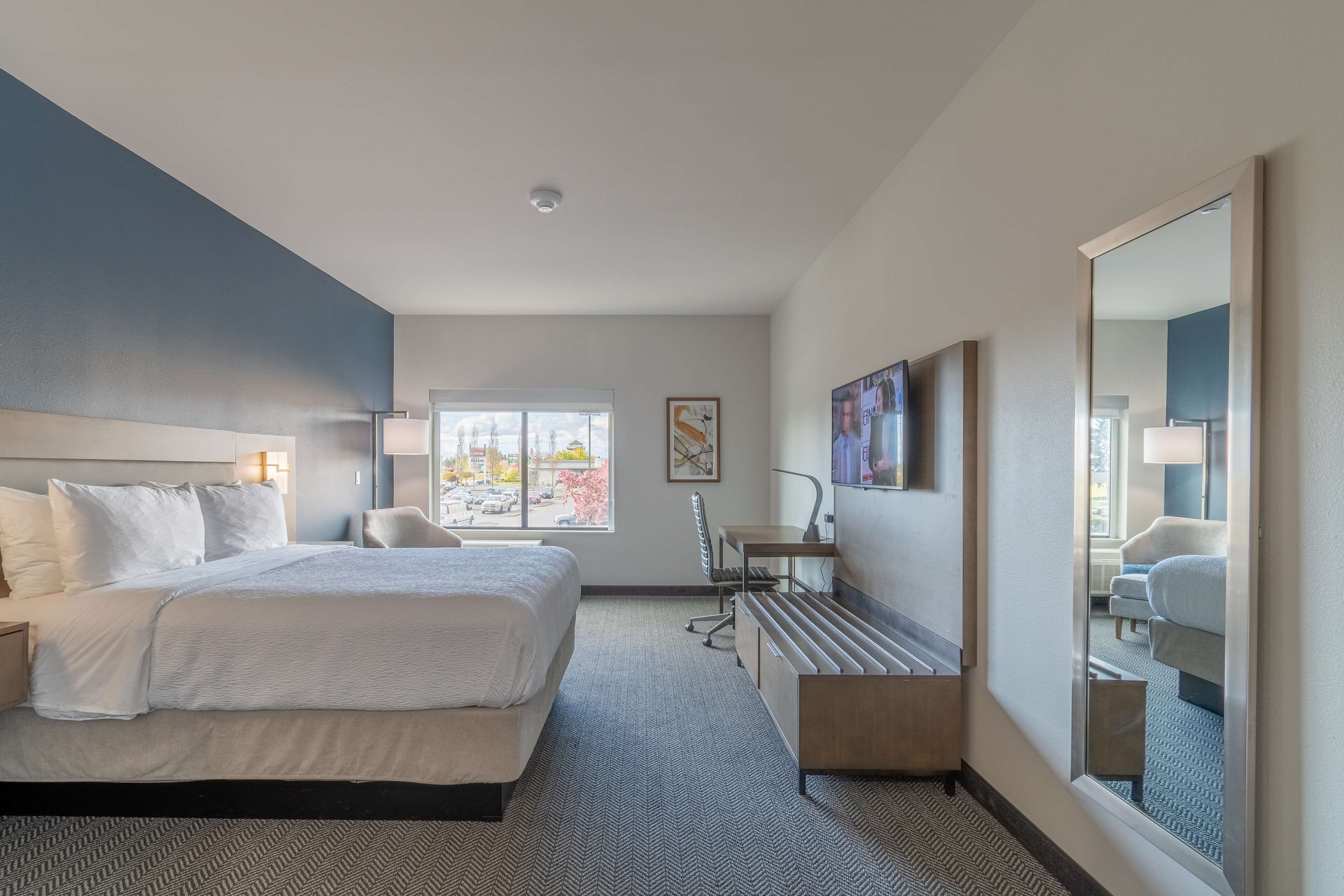A hotel room with a large bed, a desk, a chair, a window with a view, and a mirror.