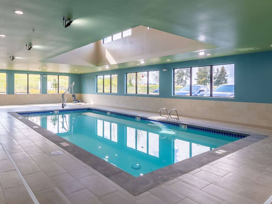 Una piscina interior con agua cristalina y azul, rodeada de ventanas que dan a vistas exteriores.